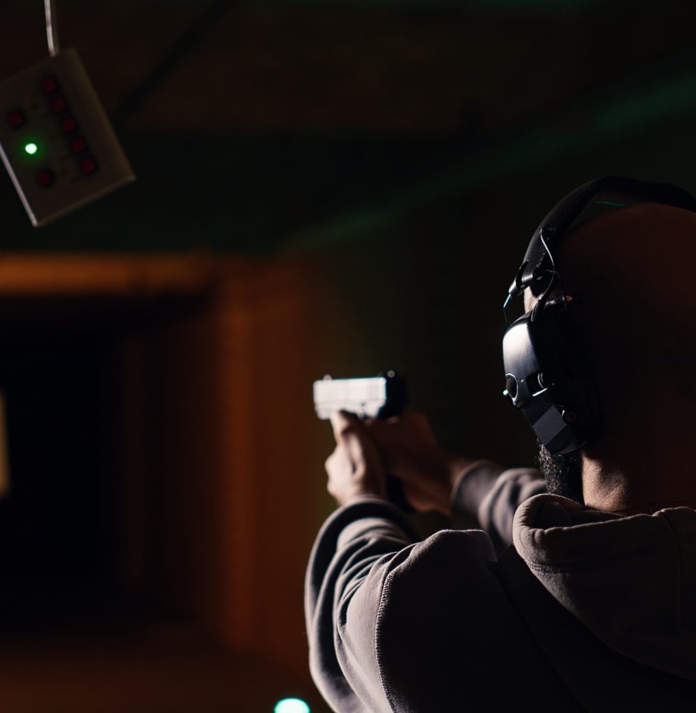 Company coworkers enjoying recreational shooting experience in firing range during teambuilding. Workplace colleagues practicing with weapons in safe shooting range environment, camera B