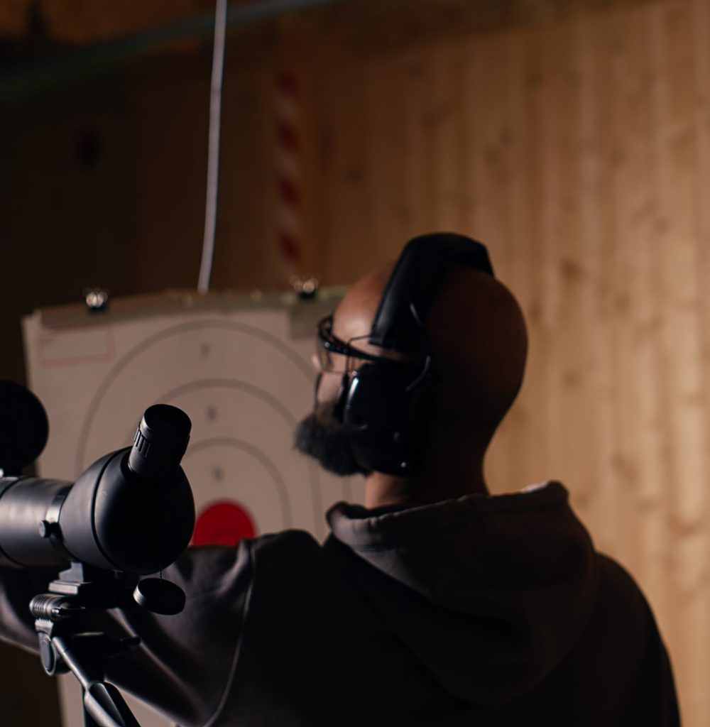 Firing range client doing shooting activity next to friends, zooming to check if he shot bullseye. Person analyzing targets shot using magnifying lens, comparing results with mates, camera B